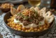 Fatteh all'agnello, pezzi di pita tostata, ceci, yogurt alla tahina e pinoli tostati.